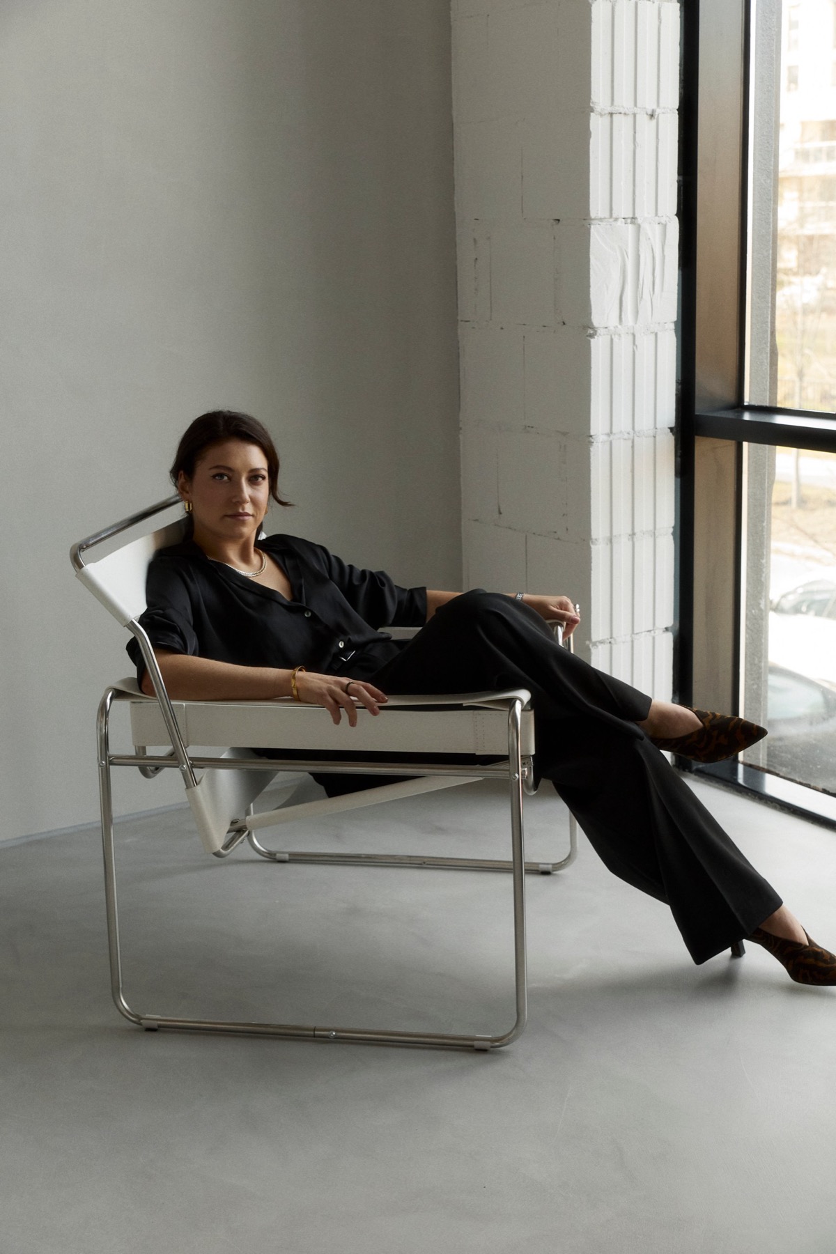 Ksenia seated in a chrome chair in a bright room with a tall window